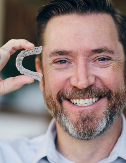 Man holding Invisalign clear aligner, Plano orthodontic care