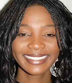 Smiling woman with braided black hair wearing silver hoop earrings against white background