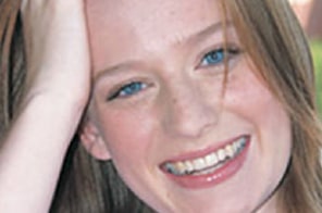 Smiling young woman with straight teeth touching her hair, displaying successful orthodontic results.