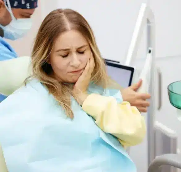 Woman in dental chair holding jaw in pain during emergency dentistry visit
