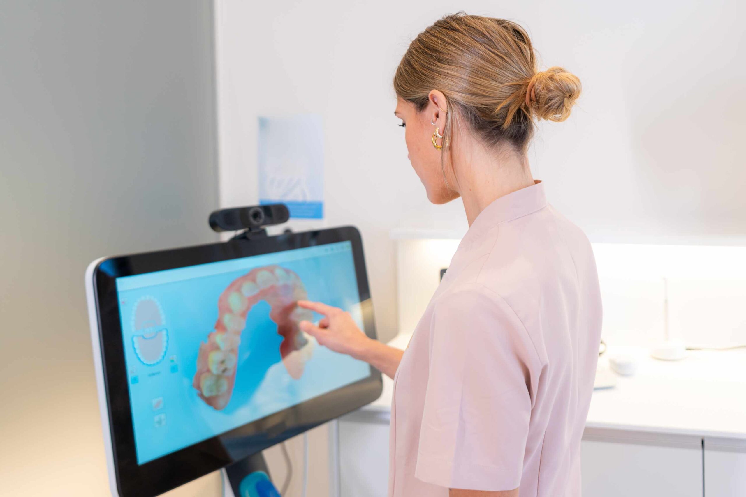 Woman viewing 3D dental scan of teeth on interactive display screen during orthodontic consultation.